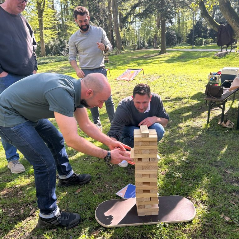 Gruppe beim Parkspiele-Teamevent in Düsseldorf: Zwei Personen spielen Jenga, andere schauen freudig zu. Teambuilding-Event im Park